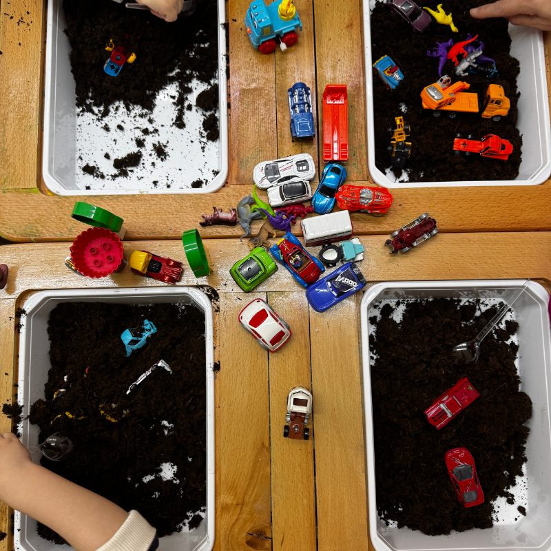 Hands go into mud kitchen with cards in a busy nursery childcare setting